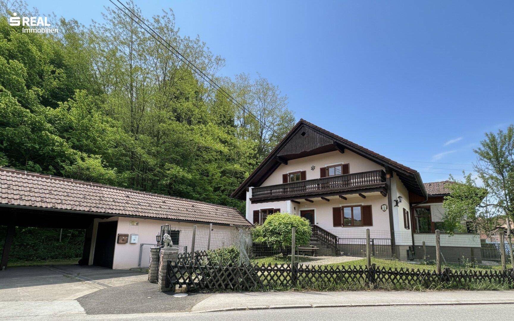 Freistehendes Haus mit Carport und Balkon, eingebettet in eine grüne Hügellandschaft.