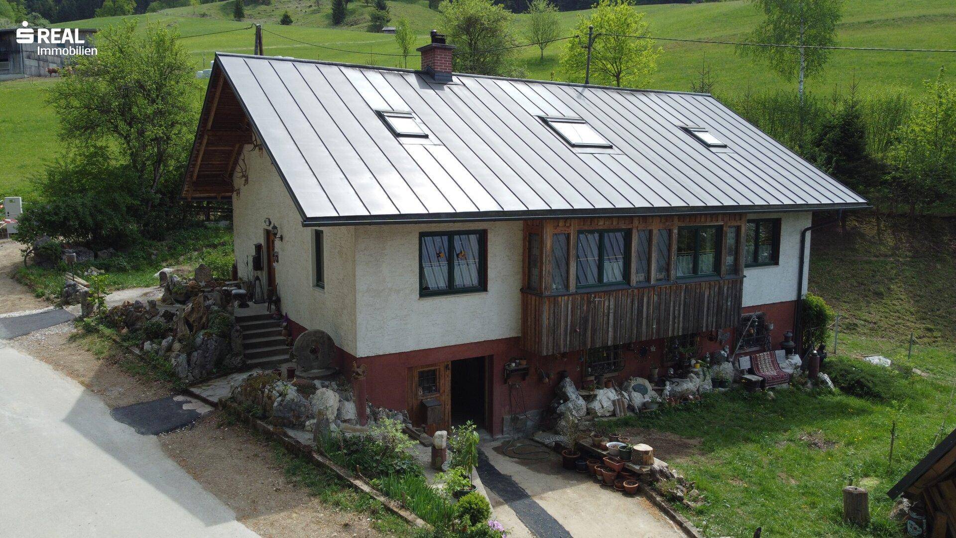 Freistehendes Haus mit Metall-Satteldach und Holzverkleidung, umgeben von Natur.