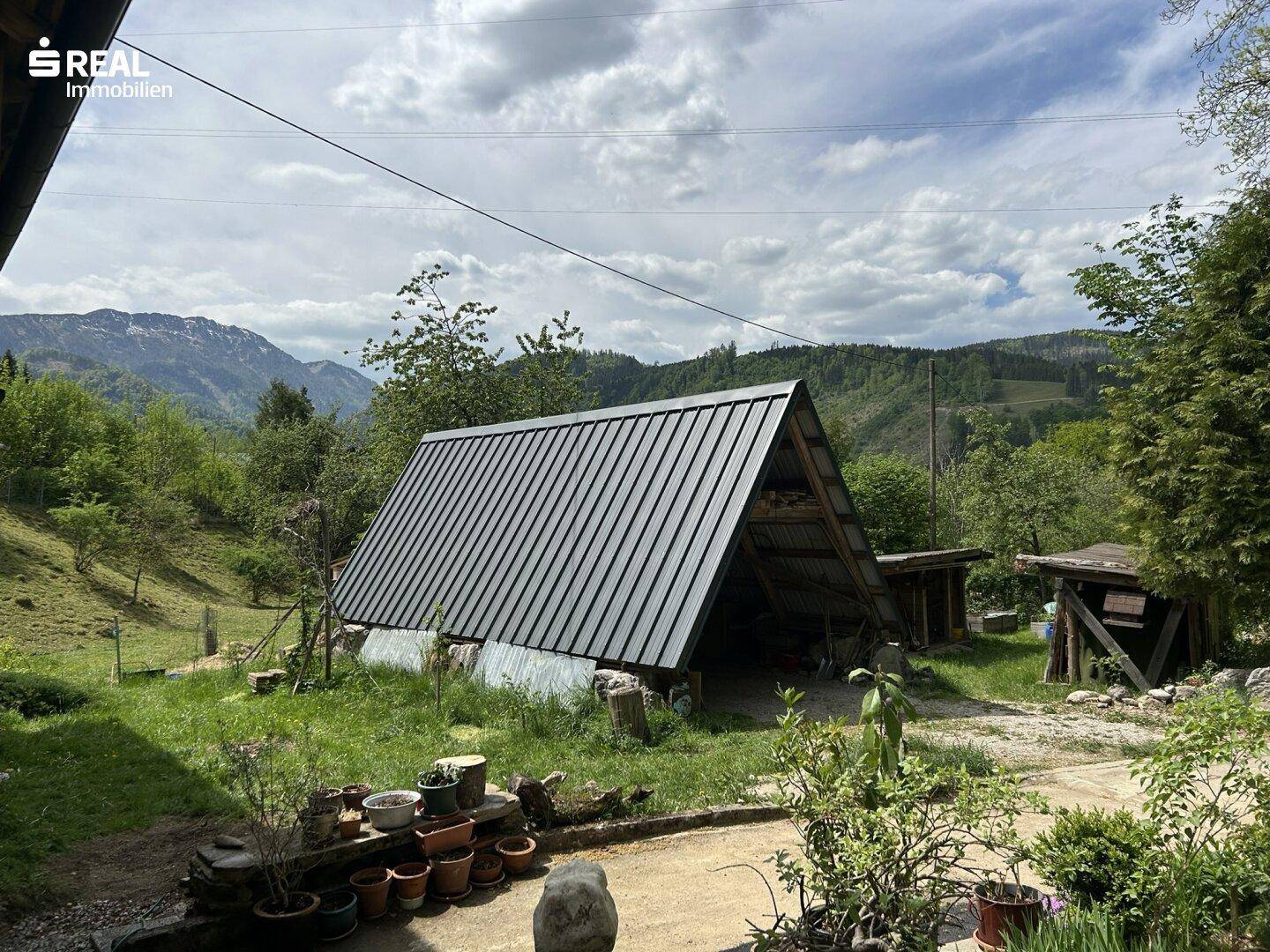 Rustikaler Holzunterstand mit Metall-Satteldach, eingebettet in die Natur.