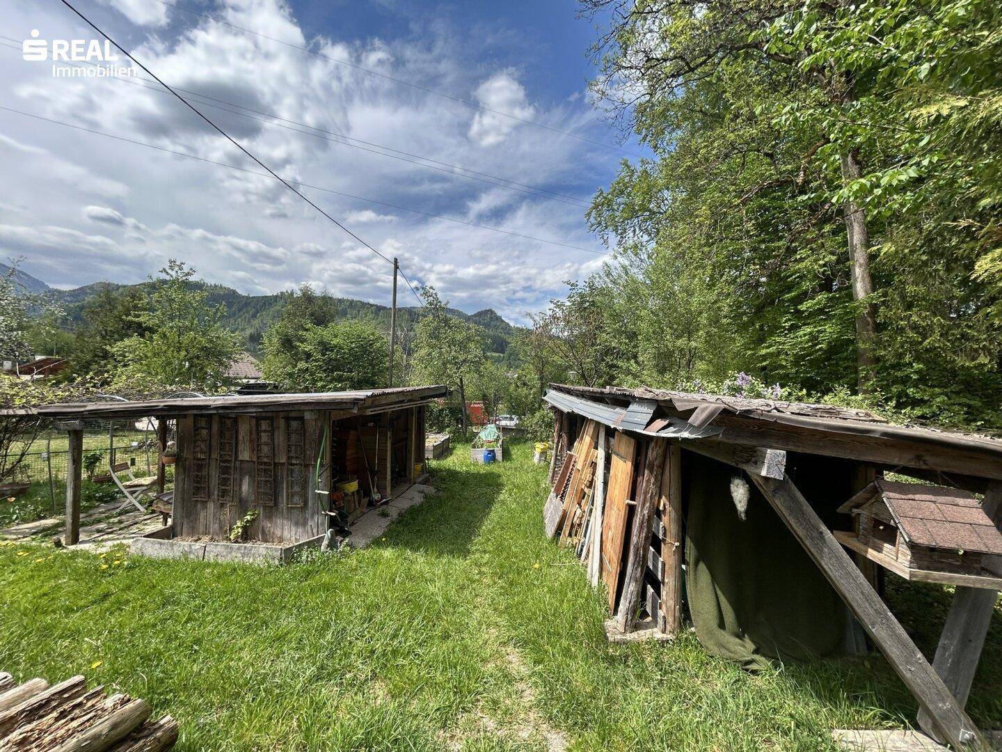 Zwei rustikale Holzschuppen im Gartenbereich, umgeben von grüner Wiese.