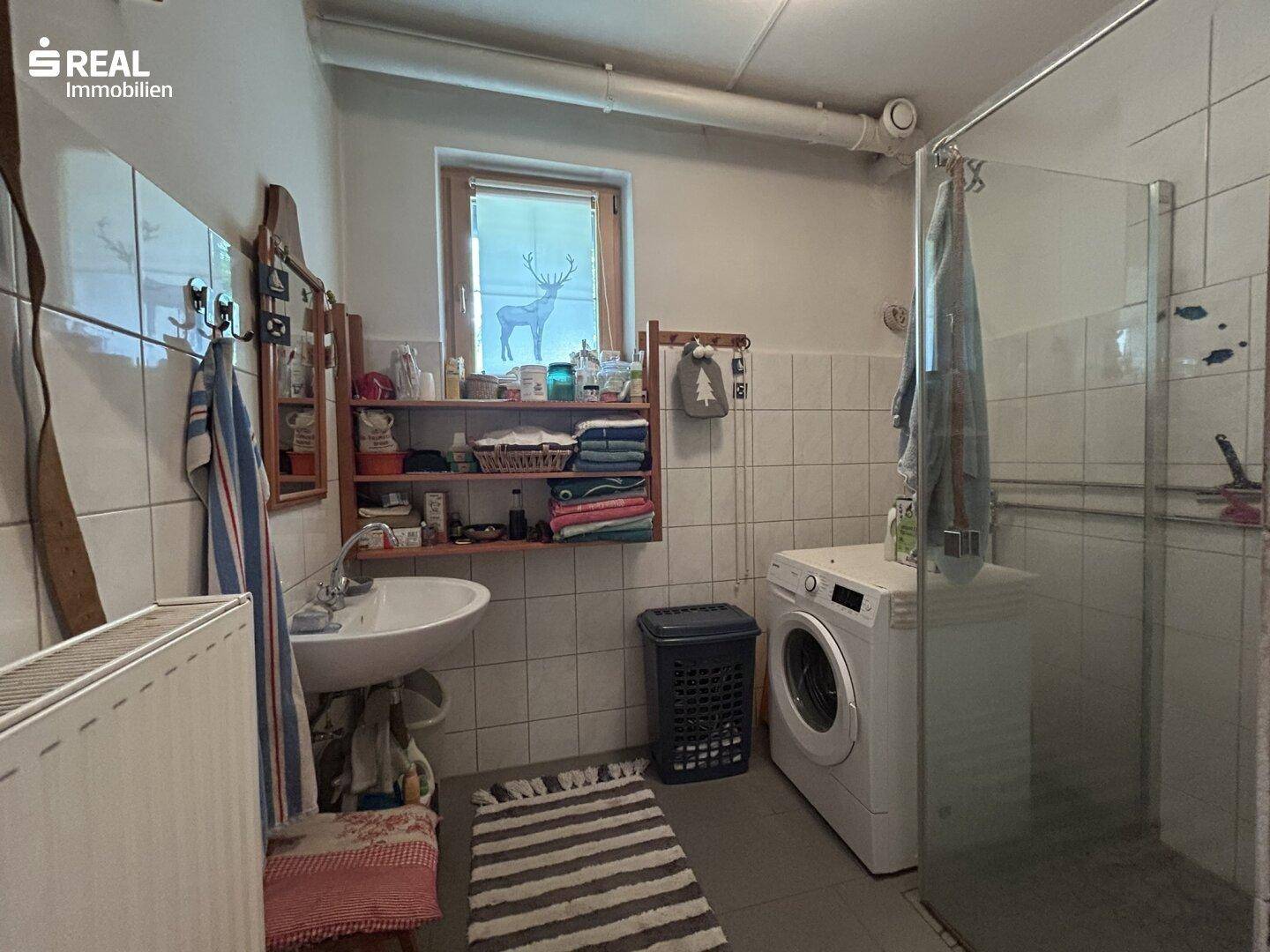 Funktionaler Waschraum mit Waschmaschine, Waschbecken und gefliesten Wänden.