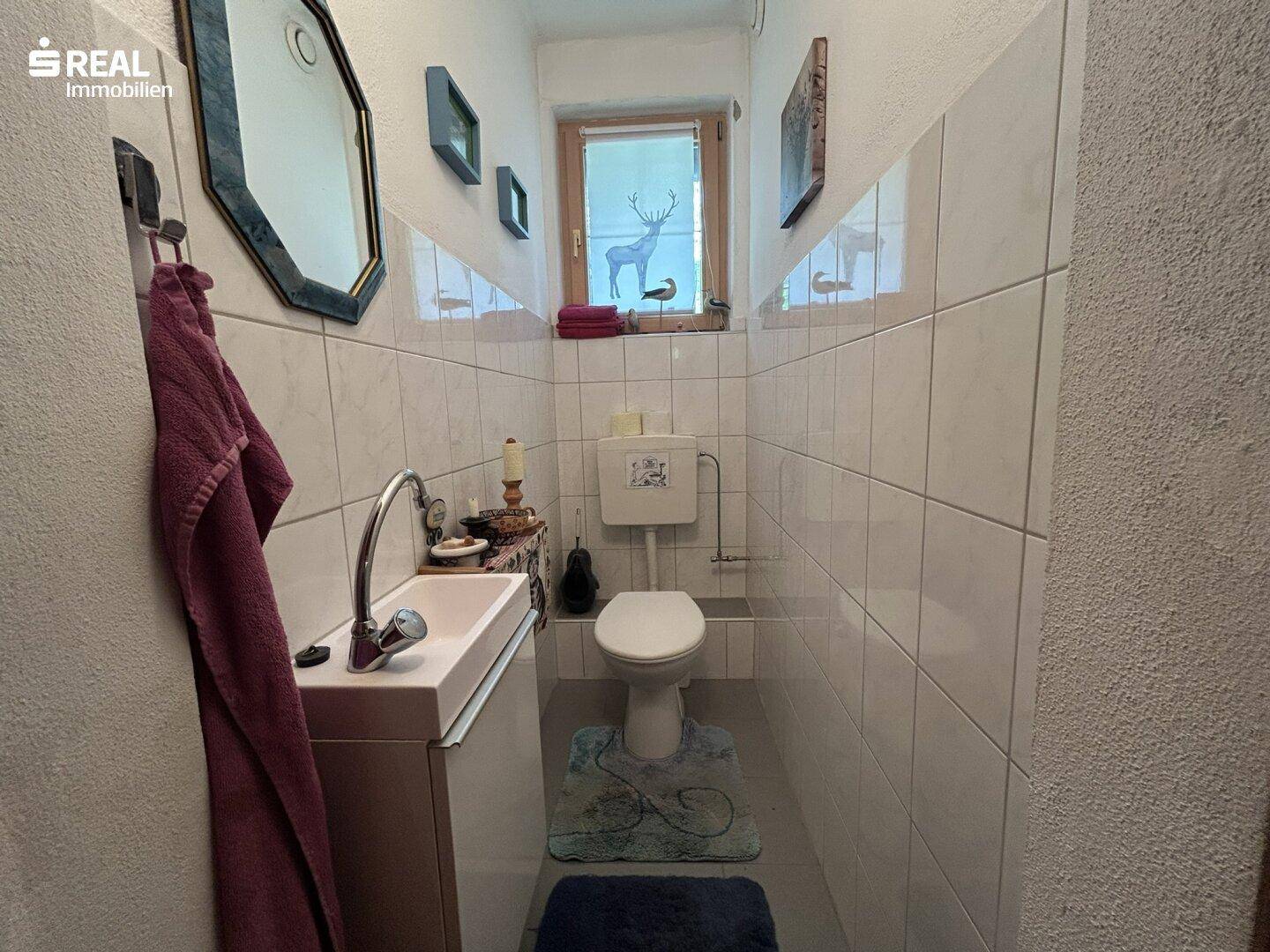 Kleines Gäste-WC mit Waschbecken, Toilette und gefliesten Wänden.