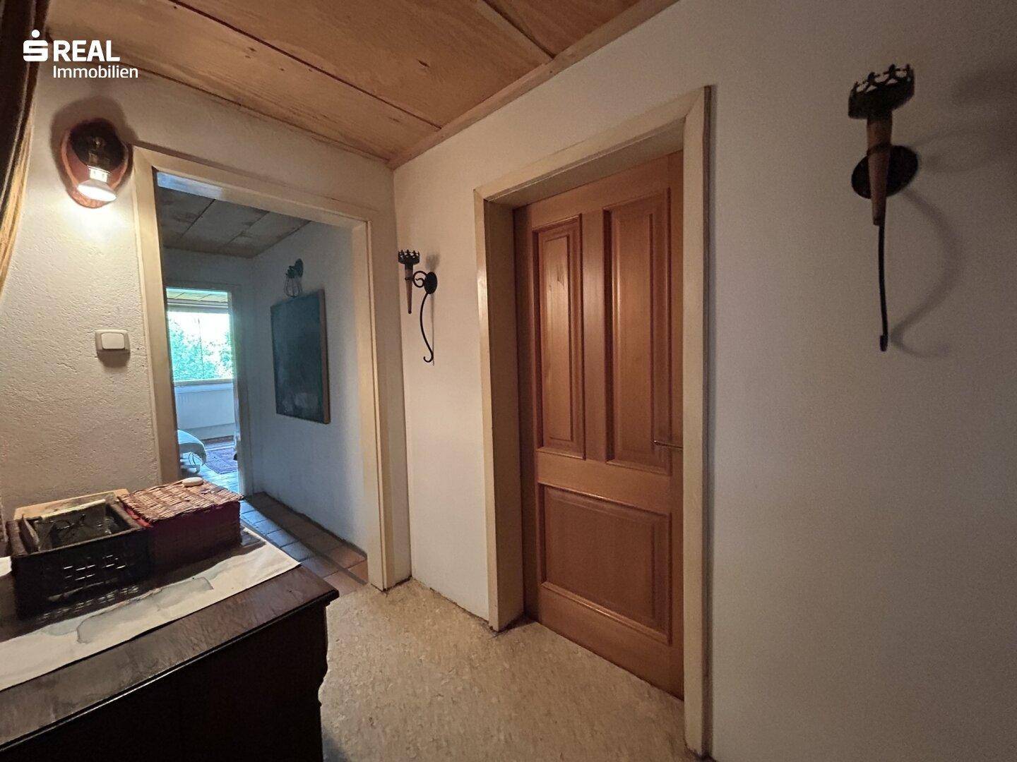 Einfacher Flur mit Holztür, Holzdecke und Wandleuchten, der zu den angrenzenden Zimmern führt.