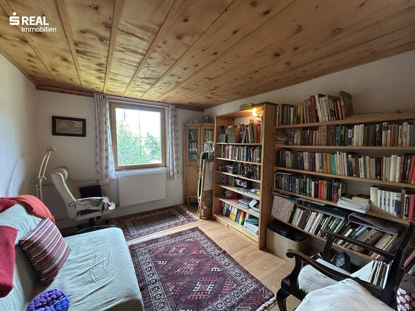 Ruhiges Arbeitszimmer mit Bücherregalen, Holzbalkendecke und Teppichboden.