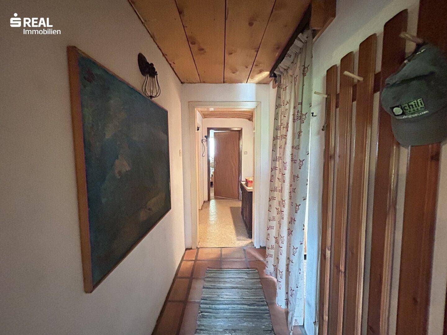 Gemütlicher Flur mit Holzbalkendecke, Terrakotta-Fliesen und Garderobe, der den Zugang zu anderen Bereichen ermöglicht.