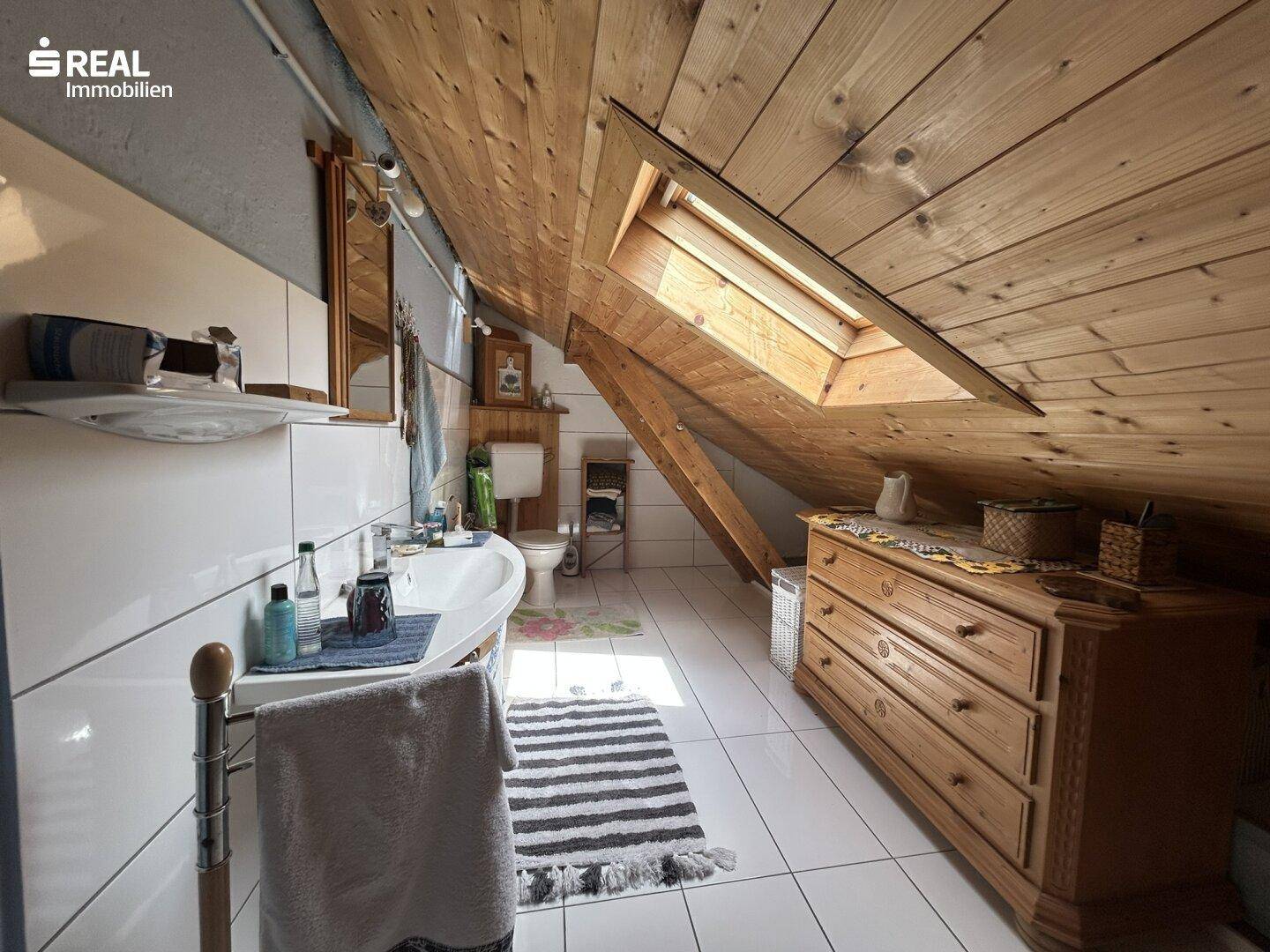 Helles Badezimmer im Dachgeschoss mit Dachschräge, Holzverkleidung, weißen Fliesen und einem Dachfenster.
