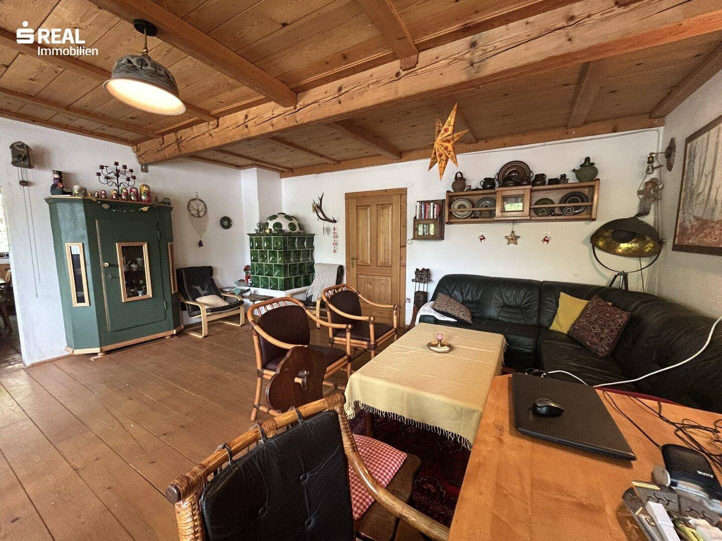 Geräumiges Wohnzimmer mit Holzbalkendecke, Kachelofen und bequemer Ledercouch.