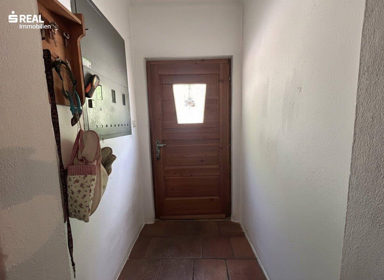 Heller Eingangsbereich mit Holztür und Terrakottafliesen, schlicht und funktional.
