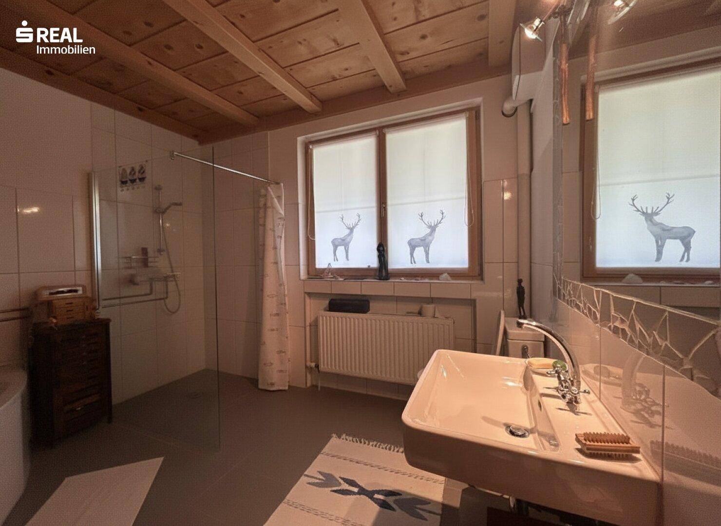 Helles Badezimmer mit Waschbecken, Dusche und Fenster mit Hirschmotiv.
