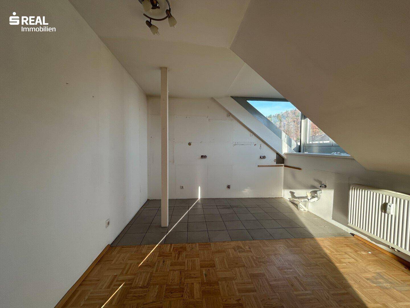 Heller Dachraum mit Parkettboden und Fliesen, schrägen Wänden und einem Fenster.