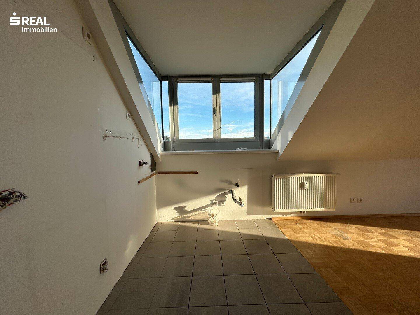 Dachraum mit großem Fenster, das viel Tageslicht hereinlässt, und Heizkörper.