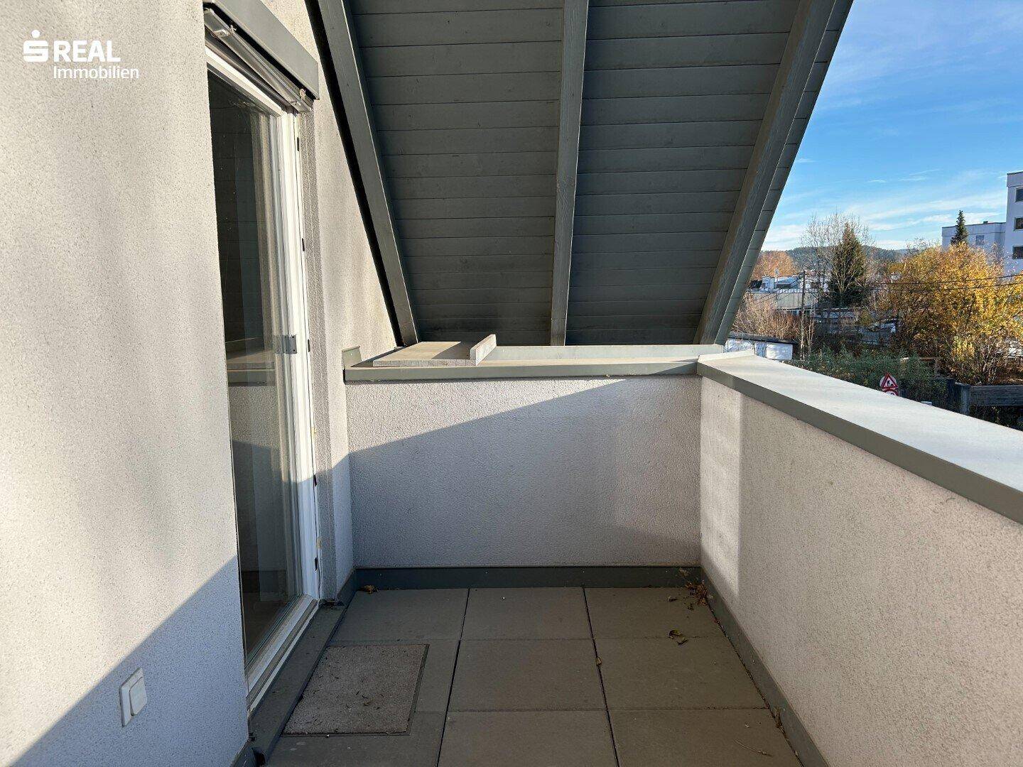 Überdachter Balkon mit Fliesenboden und weitem Blick auf die grüne Umgebung.