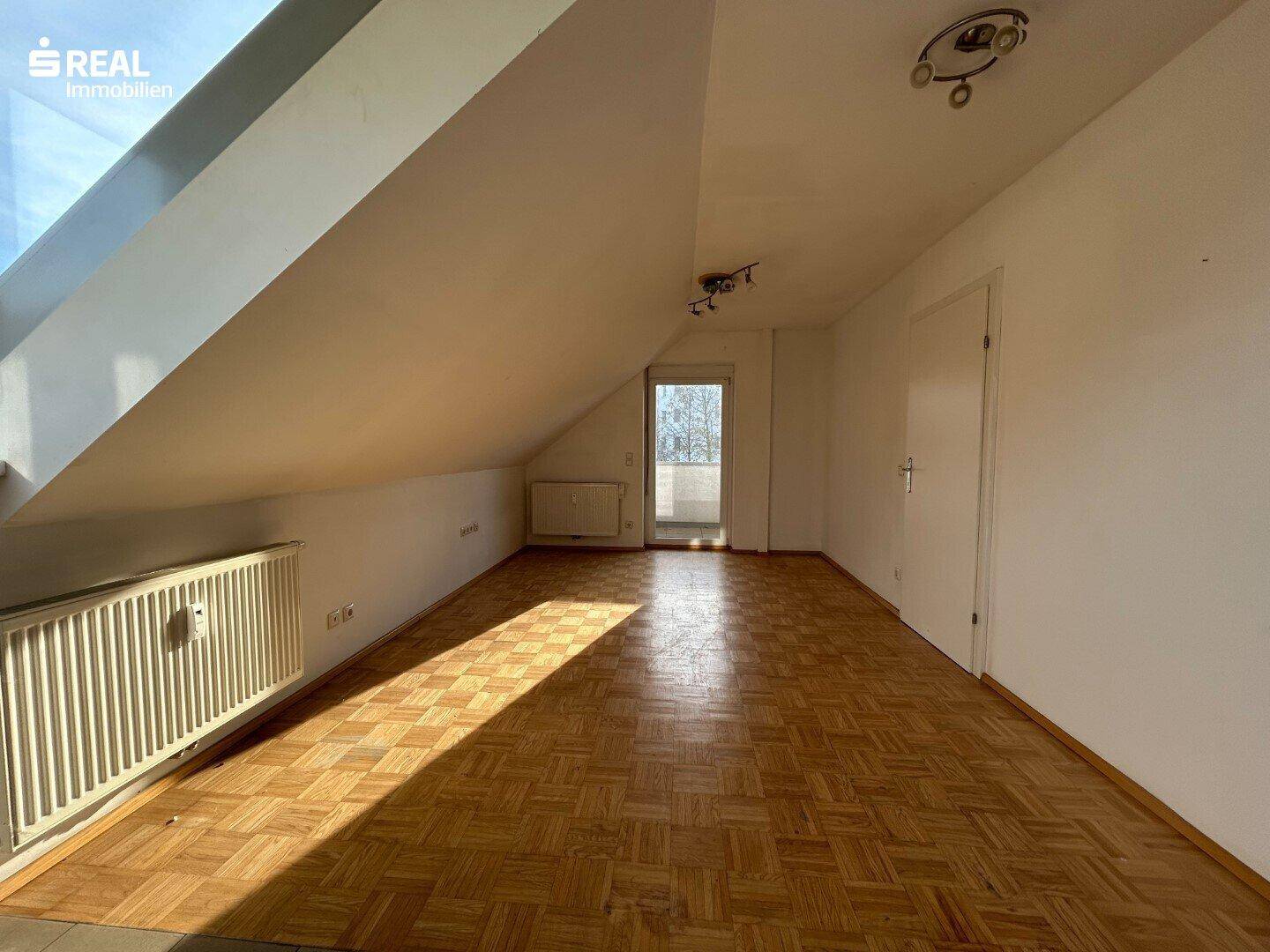 Geräumiger Dachraum mit Parkettboden, schrägen Wänden und Zugang zu einem kleinen Balkon.