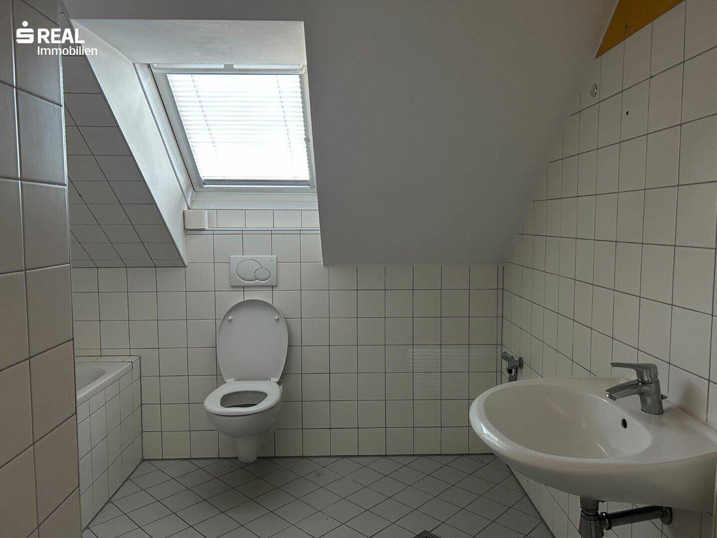 Badezimmer im Dachgeschoss mit WC, Waschbecken und Dachfenster für natürliches Licht.