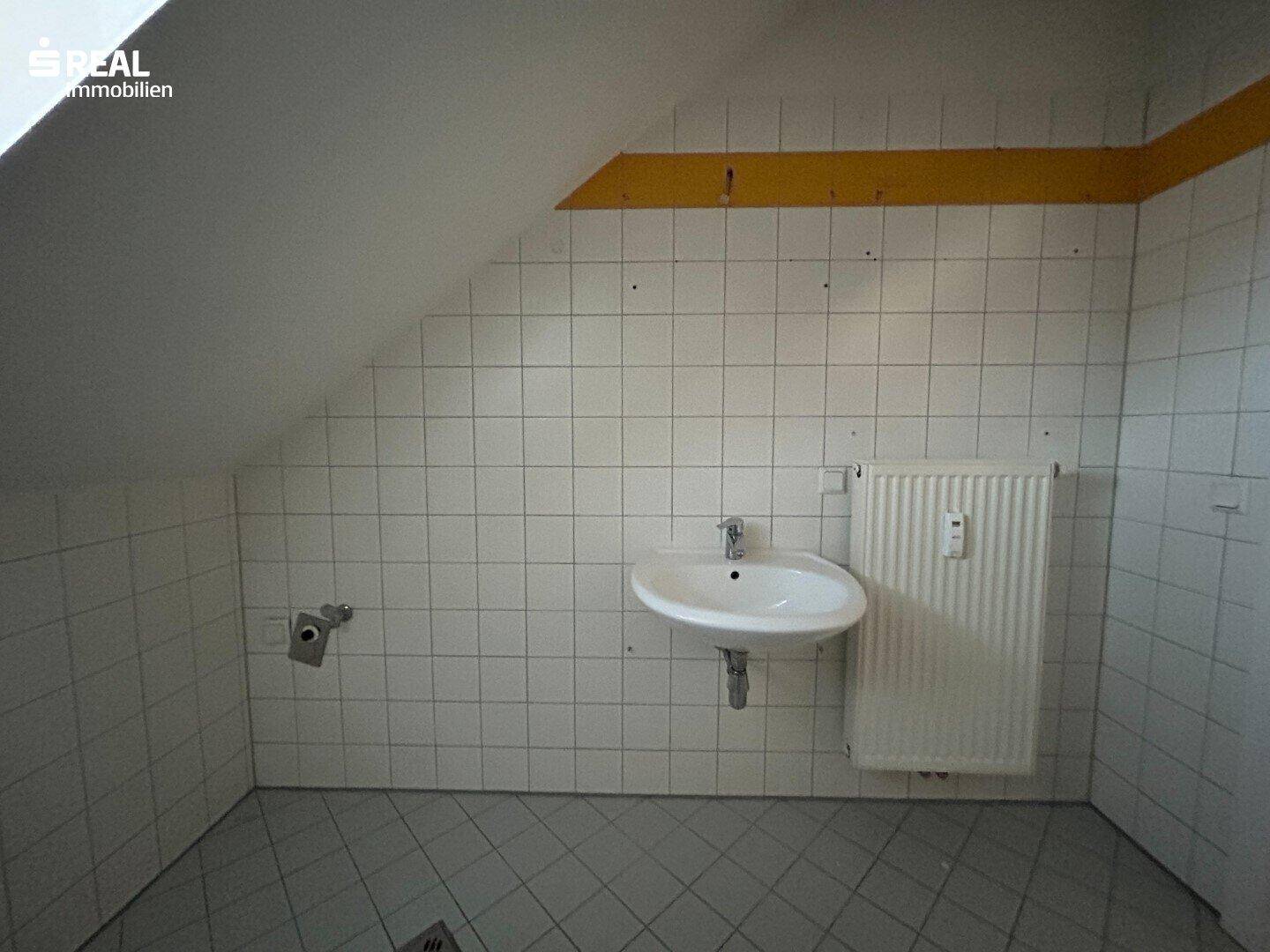 Badezimmer im Dachgeschoss mit Waschbecken, Heizkörper und schrägen Wänden, einfach ausgestattet.