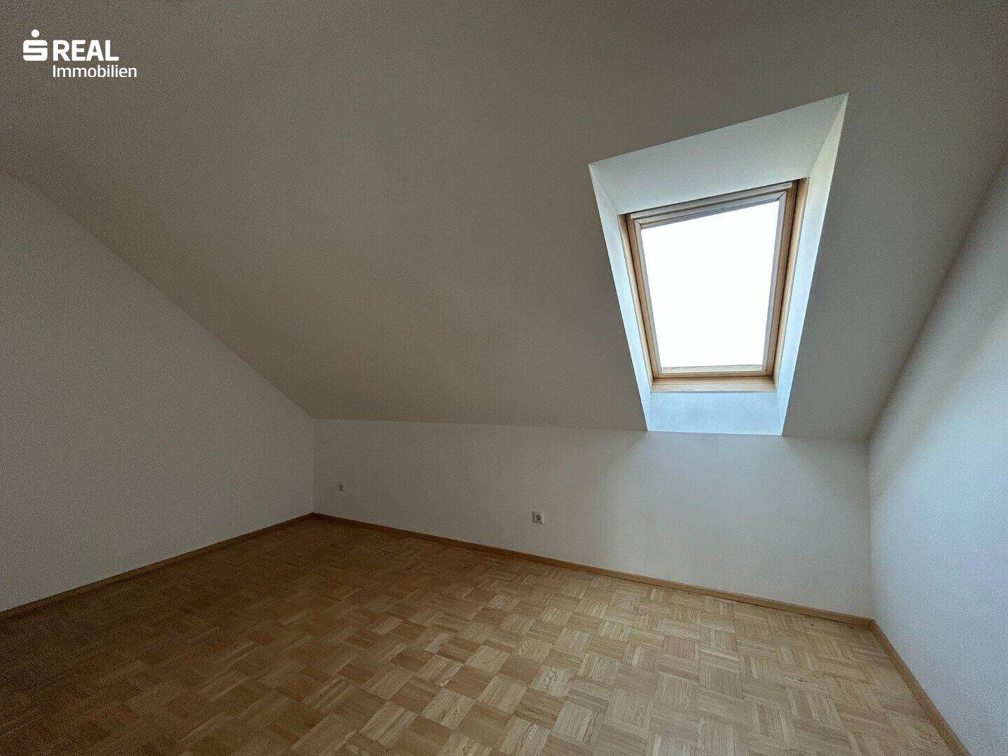 Helles Schlafzimmer im Dachgeschoss mit Parkettboden und einem Dachfenster.