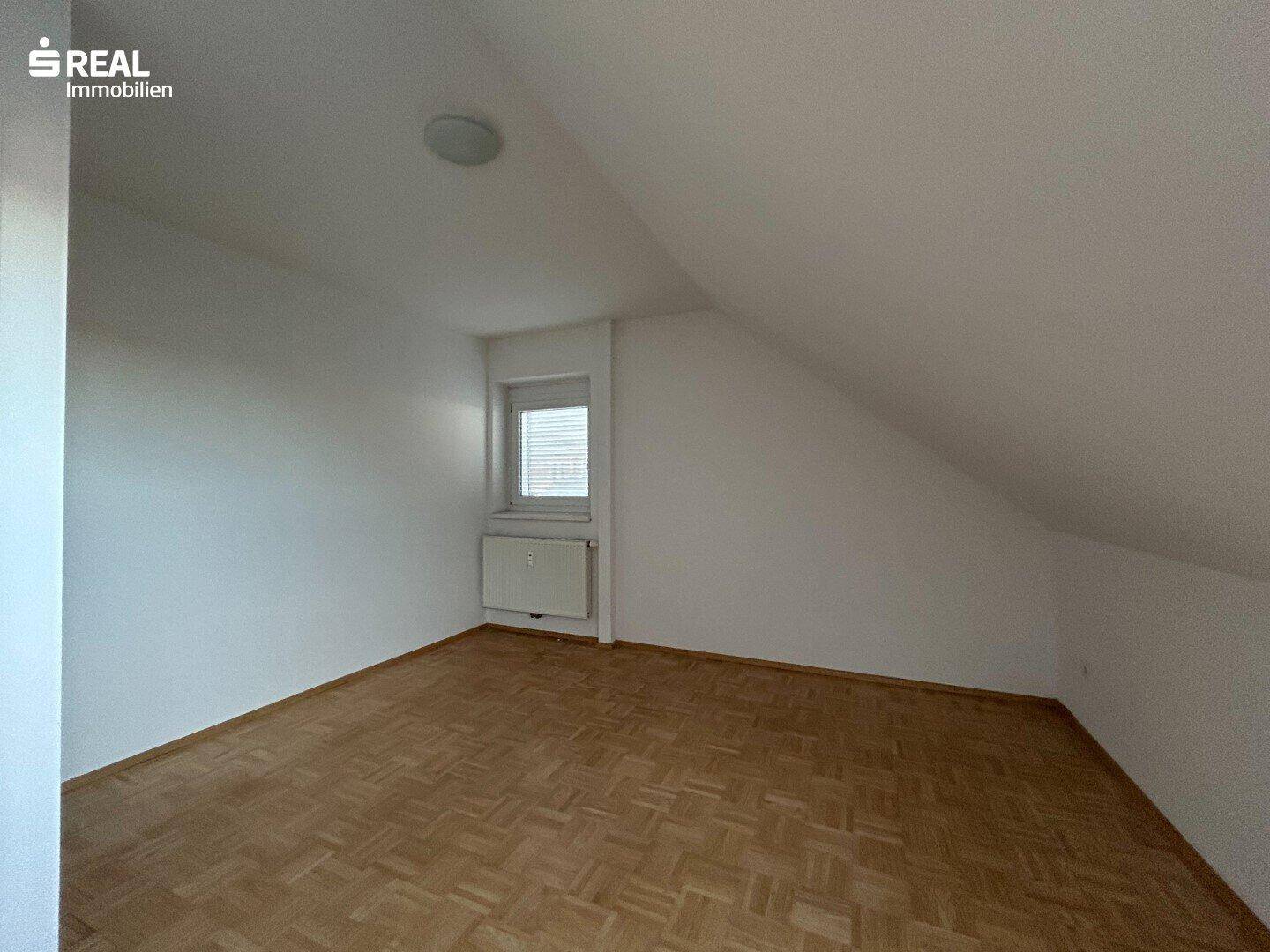 Dachzimmer mit Parkettboden, schrägen Wänden und einem kleinen Fenster.