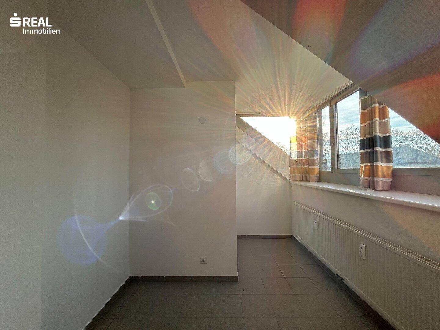 Sonnenlichtdurchfluteter Dachraum mit Fliesenboden und großen Fenstern.