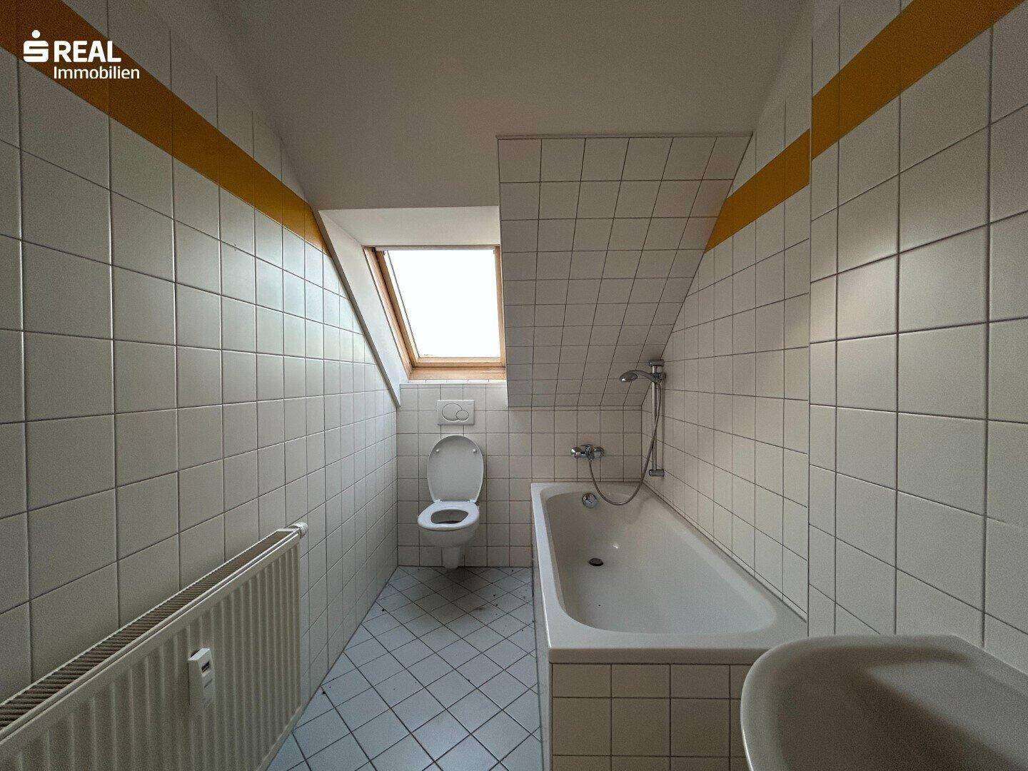 Badezimmer im Dachgeschoss mit Badewanne, WC und Heizkörper, mit schräger Decke.