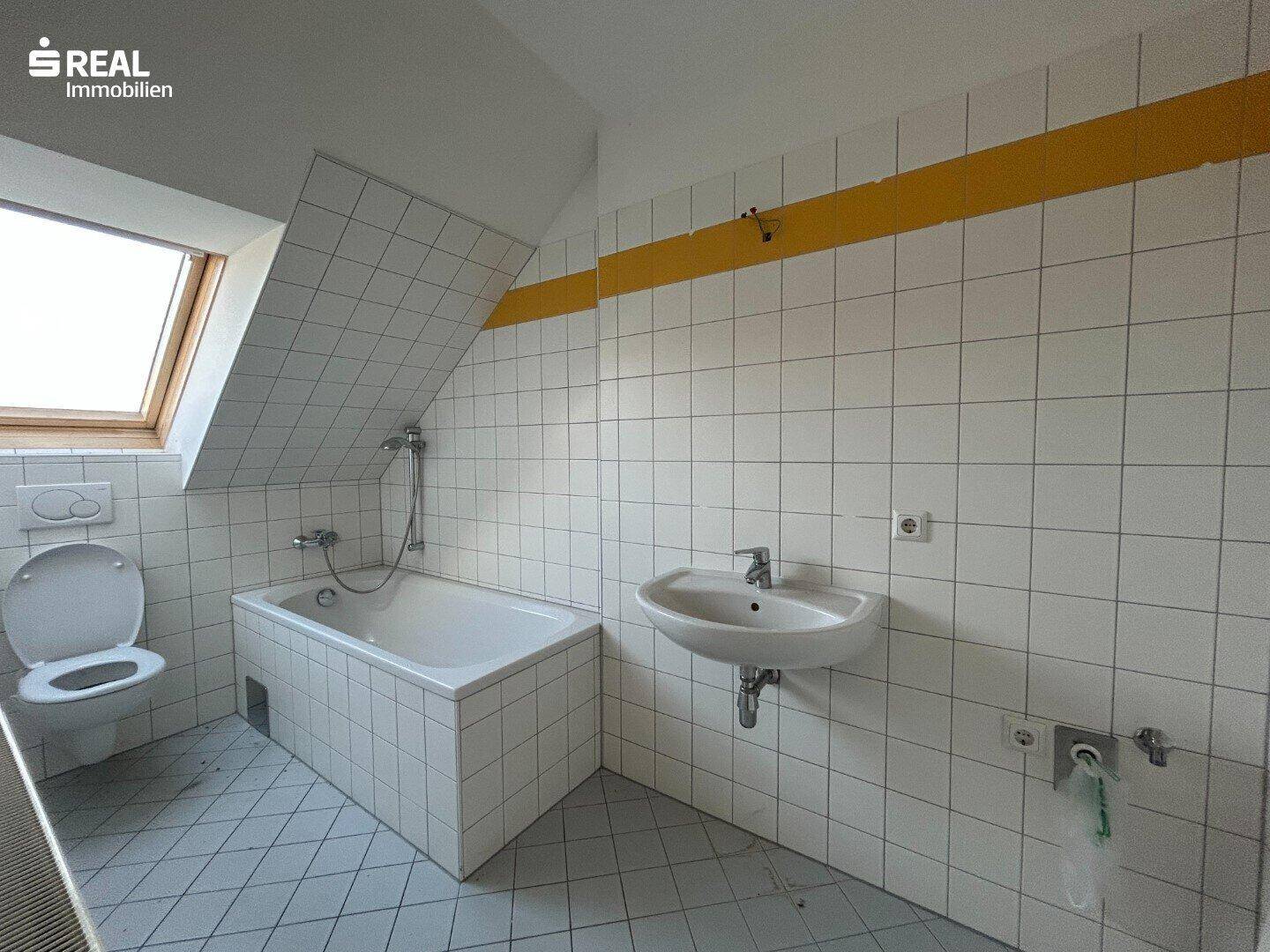 Badezimmer im Dachgeschoss mit Badewanne, Waschbecken und Dachfenster, gut gepflegt.