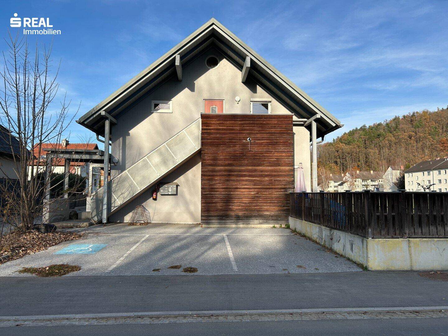 Vorderansicht des Gebäudes mit Holzelementen an der Fassade und Parkplätzen.