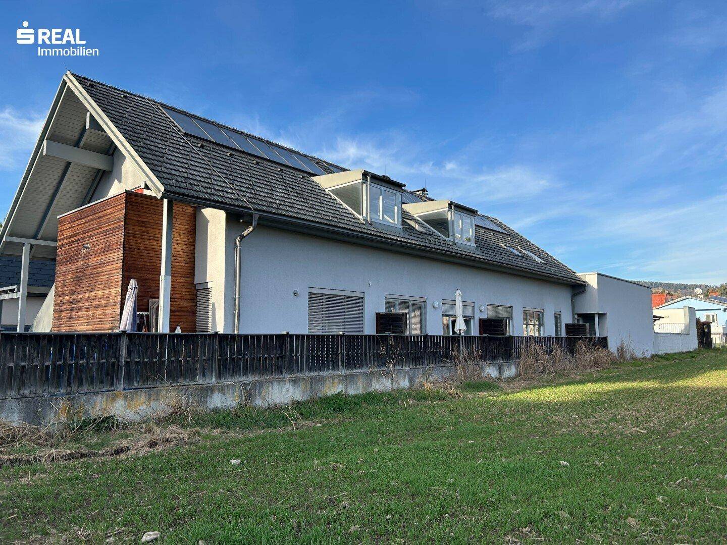 Rückansicht des Gebäudes mit Solarpaneelen auf dem Dach und einer Rasenfläche im Vordergrund.