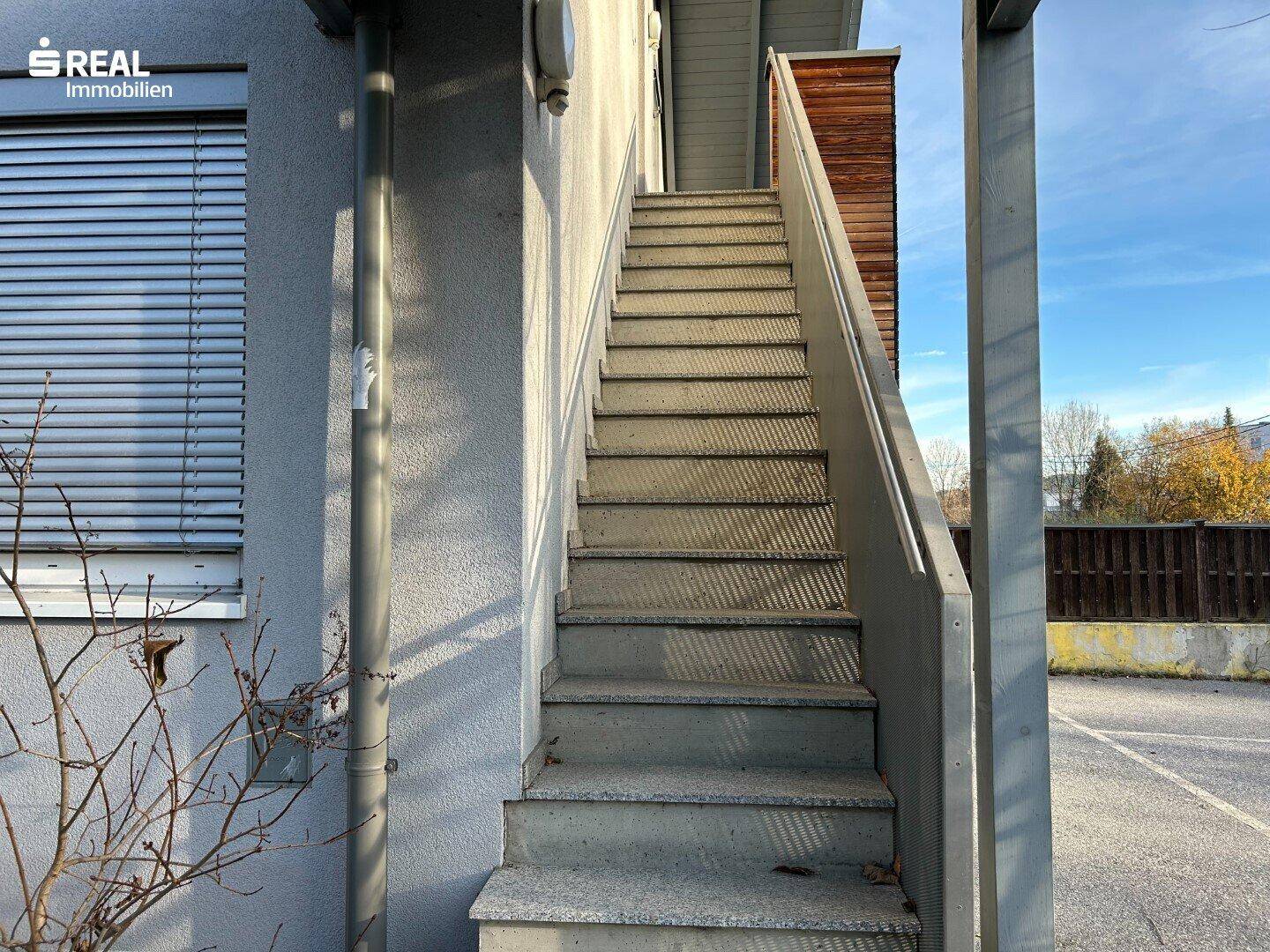 Außentreppe führt zum Eingang des Gebäudes mit Jalousien an den Fenstern.