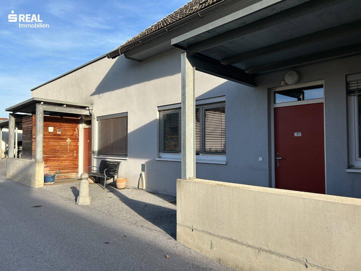 Eingangsbereich des Gebäudes mit überdachtem Zugang und einer kleinen Bank.