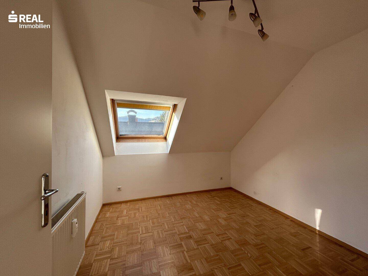 Helles Schlafzimmer im Dachgeschoss mit Parkettboden und einem Dachfenster.