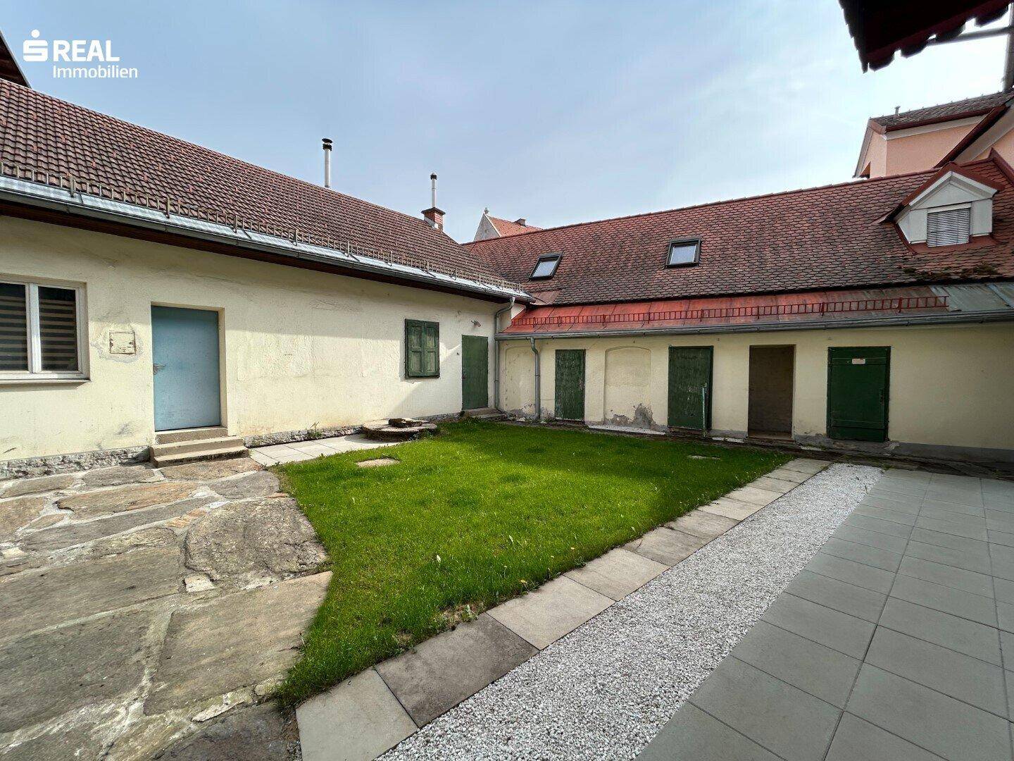 Innenhof mit Rasenfläche und gepflasterten Wegen, umgeben von Gebäuden.