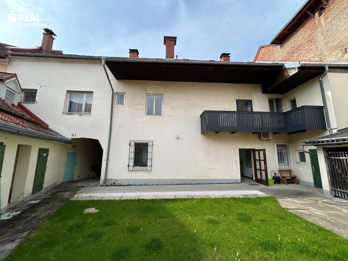 Hinterhofansicht mit kleinem Balkon und Rasenfläche, umgeben von Gebäudefassaden.