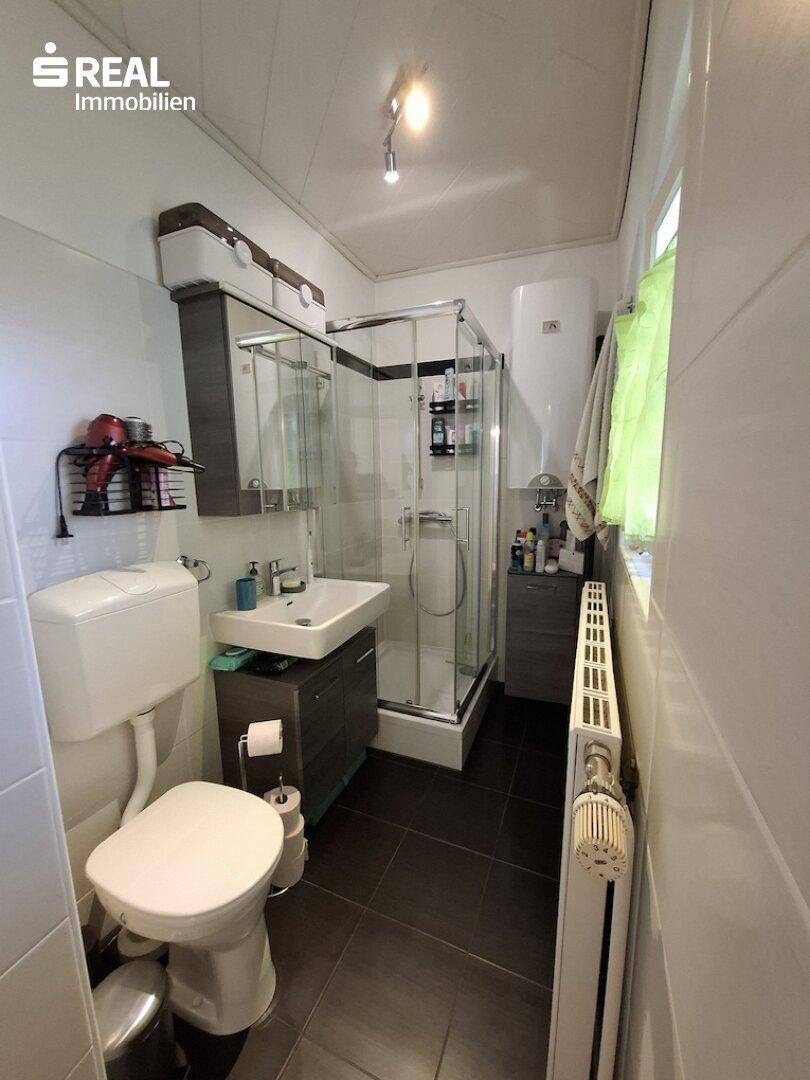 Modernes Badezimmer mit Dusche, Waschbecken und Toilette, ausgestattet mit dunklen Fliesen.