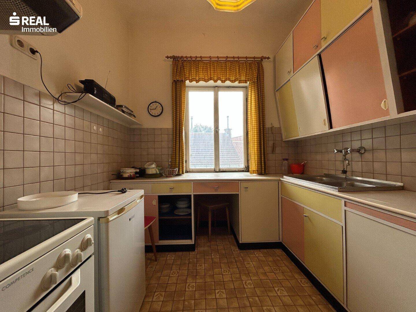 Vintage-Küche mit bunten Schränken, Fliesen und einem Fenster mit Blick nach draußen.