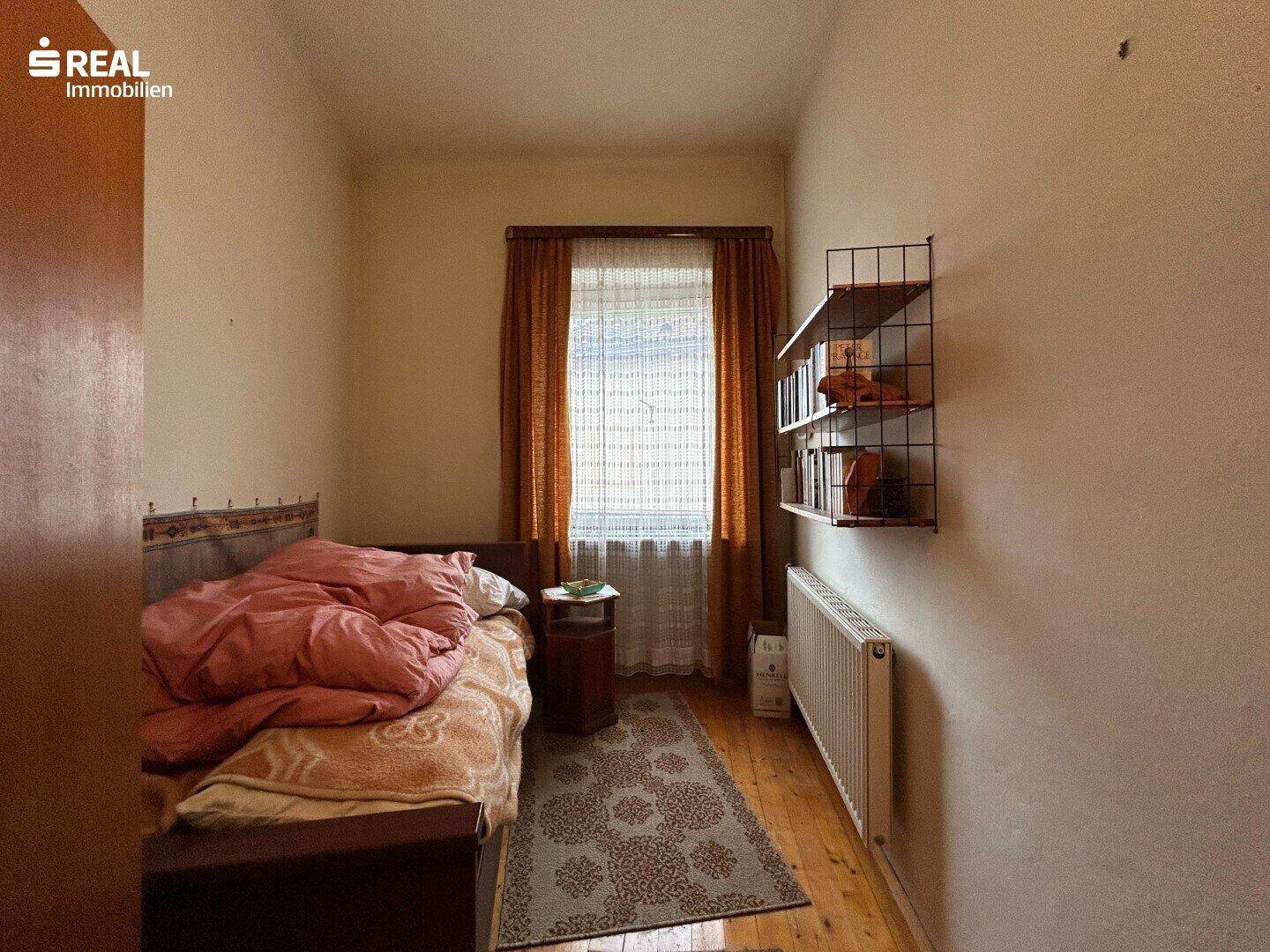 Gemütliches Schlafzimmer mit Holzboden, Einzelbett und einem kleinen Regal an der Wand.