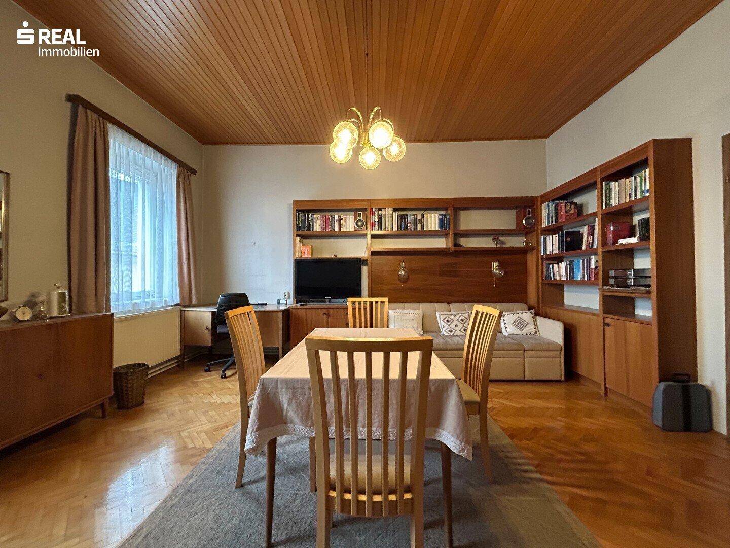 Wohn-Esszimmer mit Holztäfelung an der Decke, Parkettboden und großem Esstisch.