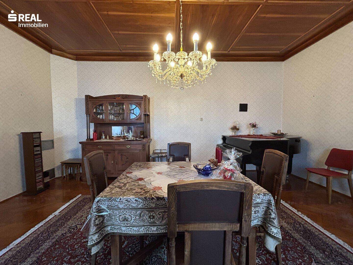 Großzügiges Esszimmer mit Holzboden, Kronleuchter und einem Klavier im Hintergrund.