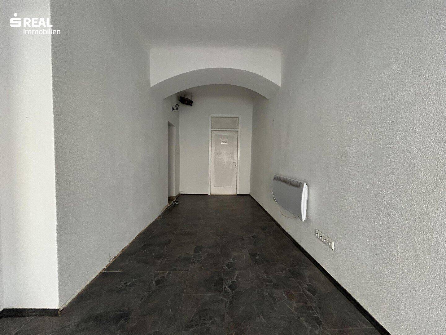 Leerer Geschäftsraum mit dunklem Fliesenboden und gewölbter Decke im Eingangsbereich.