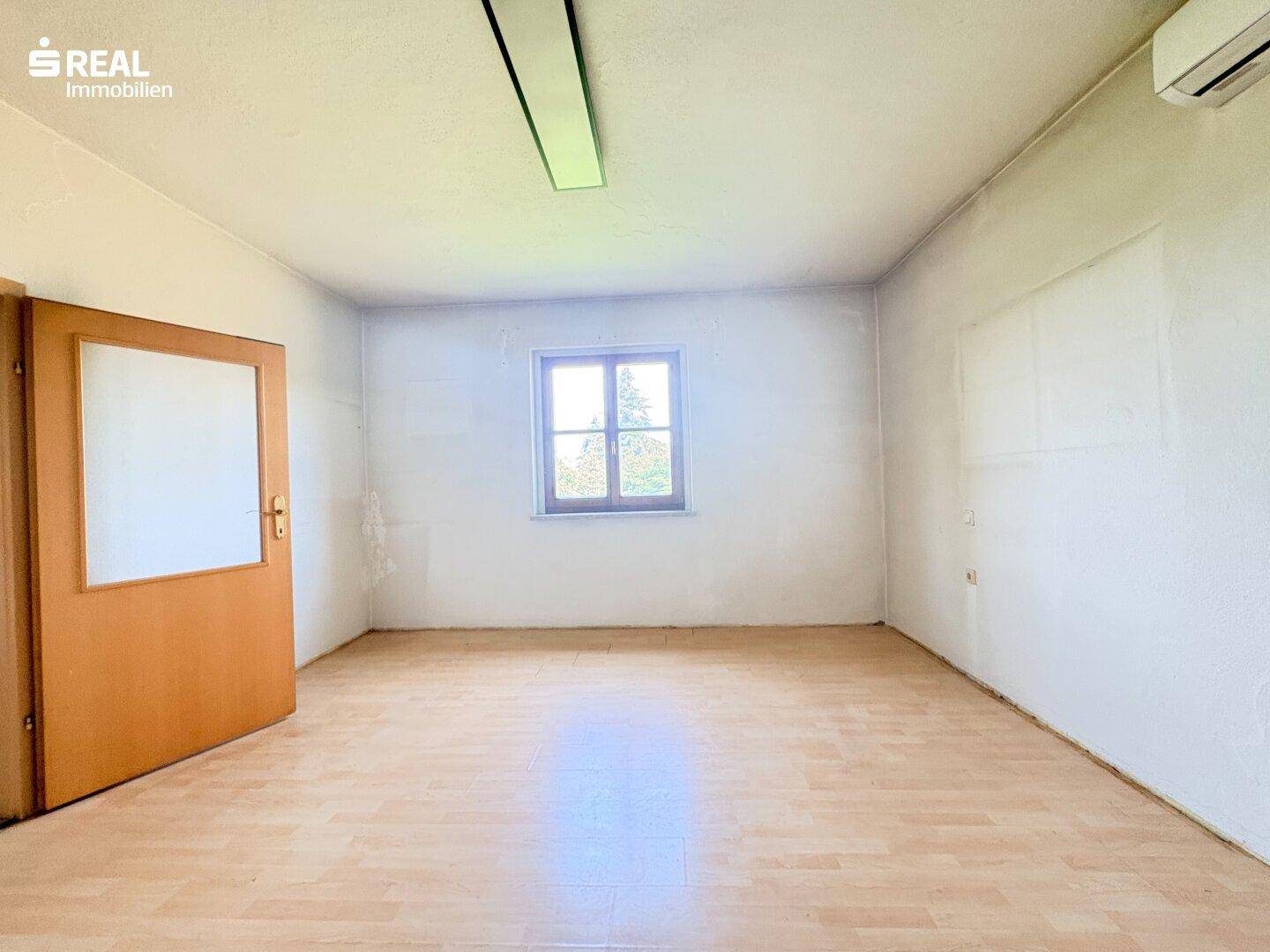 Funktionaler Raum mit Laminatboden, Fenster und Klimaanlage, ideal als Büro oder Gästezimmer.