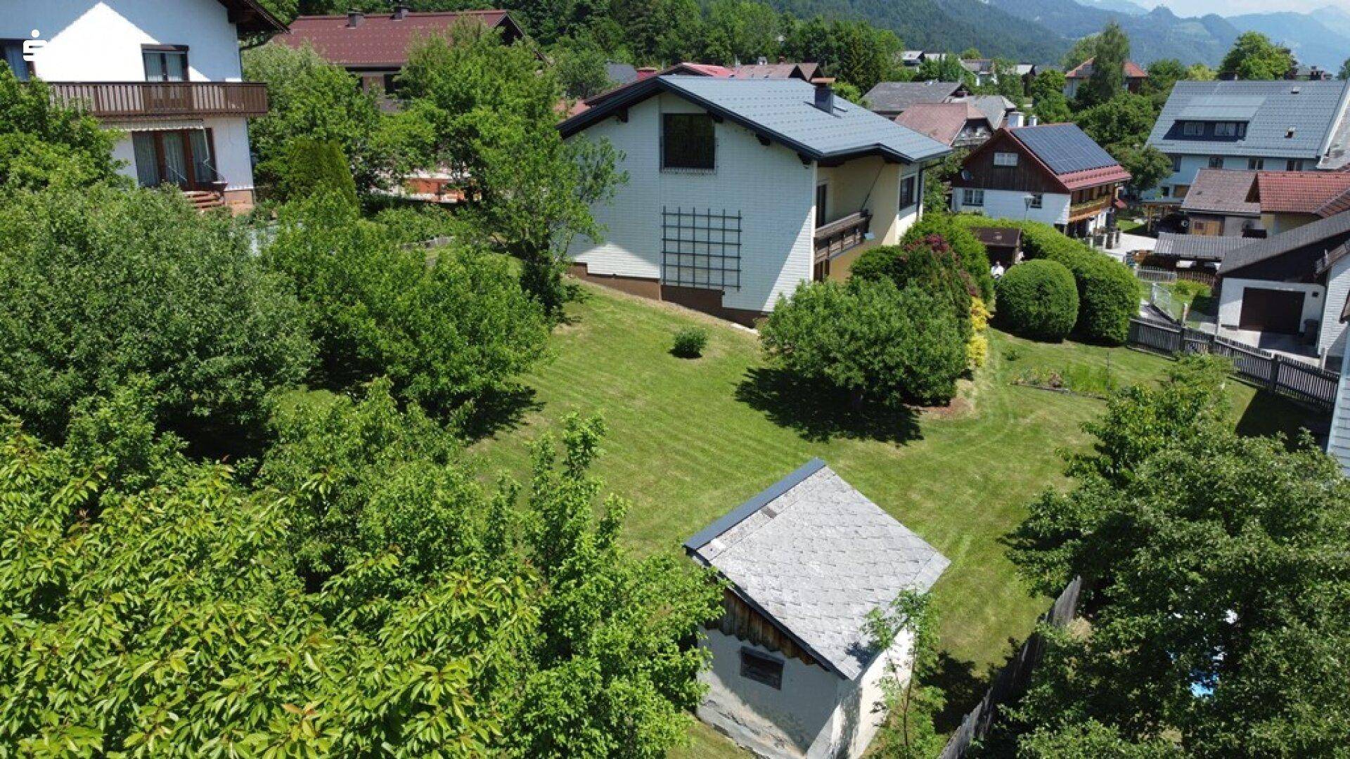 Weitläufiger Gartenbereich mit Rasenfläche, Bäumen und einem kleinen Gartenhaus, umgeben von Natur.