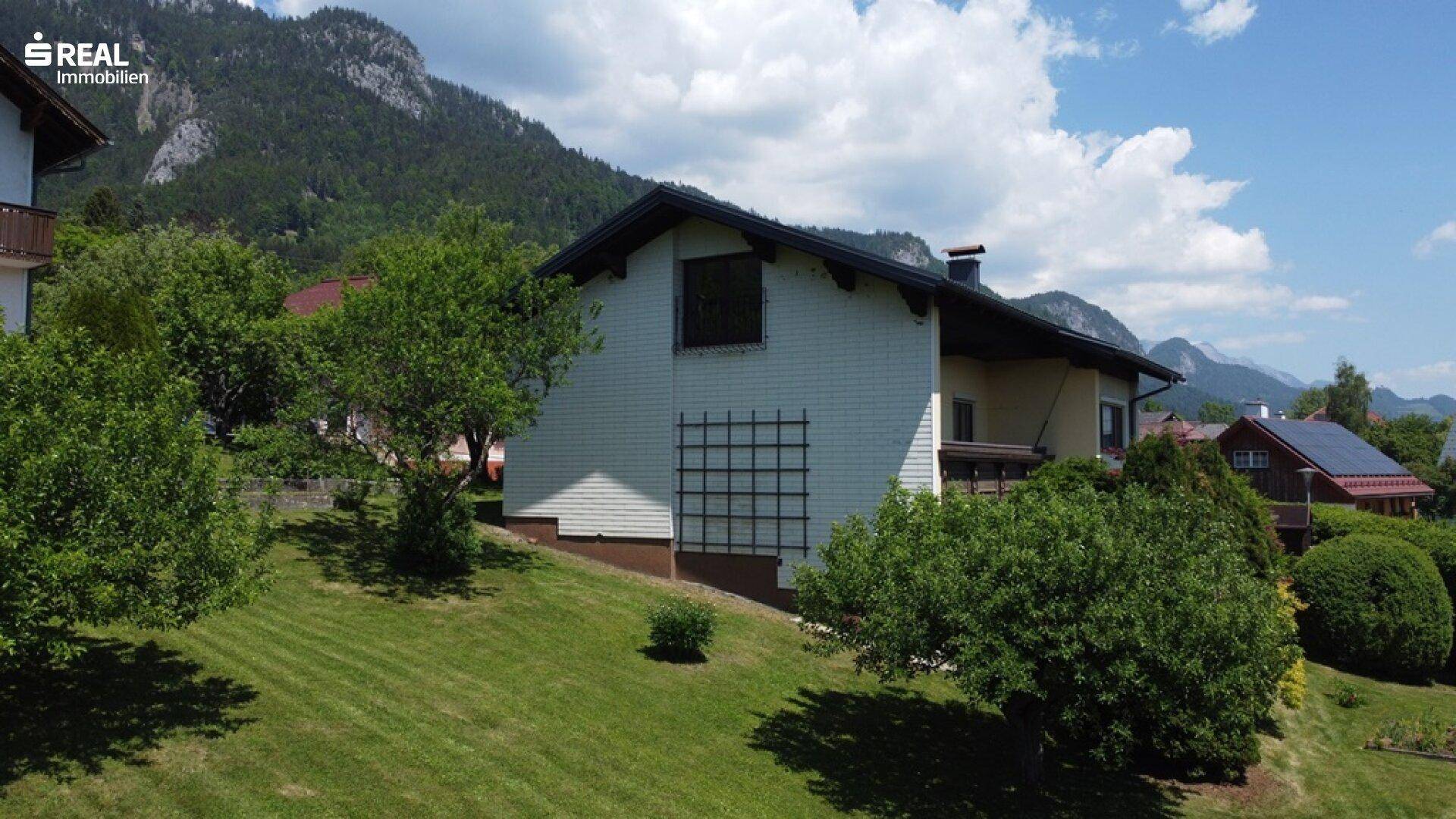 Seitenansicht des Hauses mit grüner Rasenfläche und beeindruckendem Bergblick im Hintergrund.