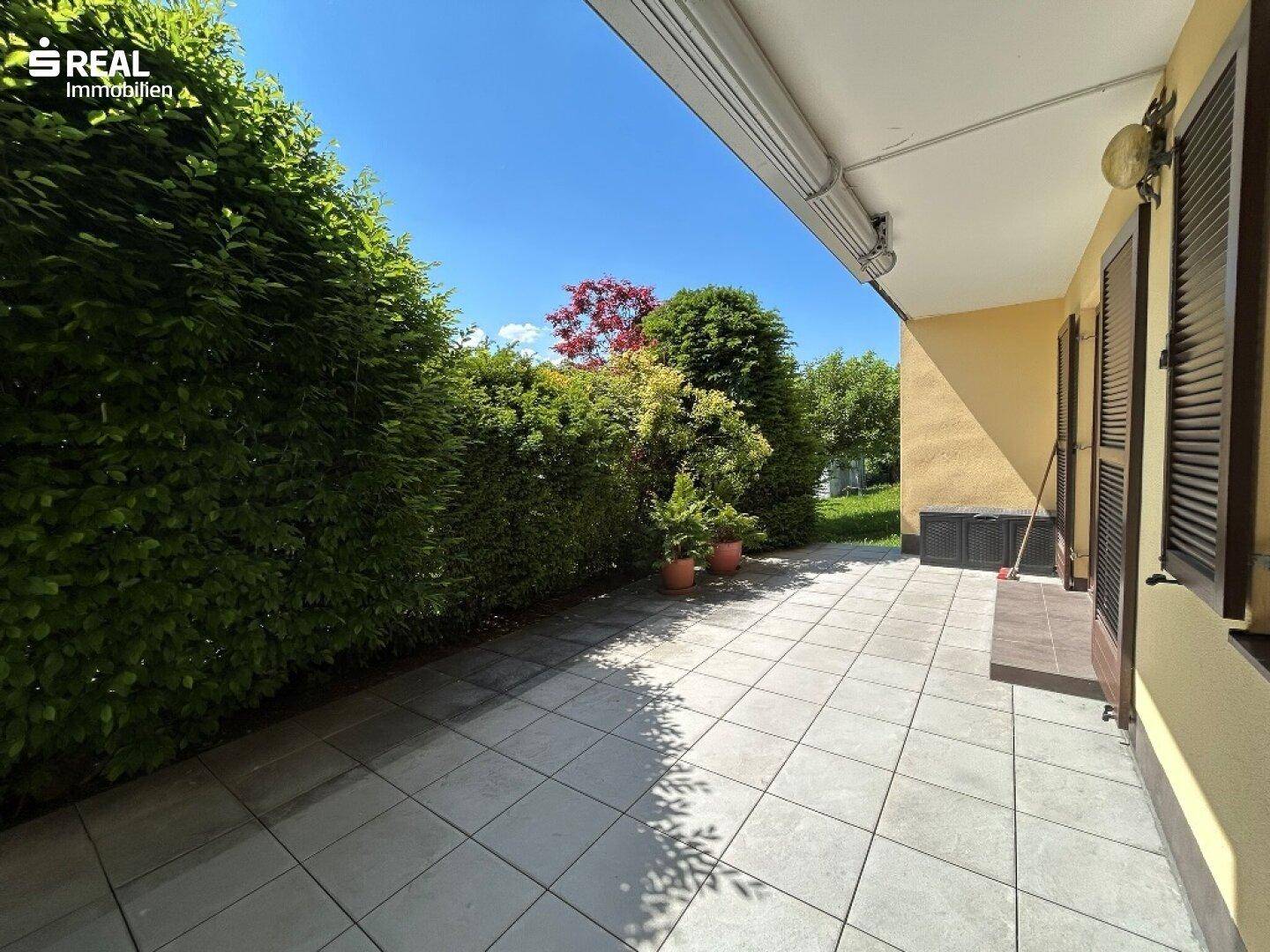 Gedeckte Terrasse mit Fliesenboden und Hecke, ideal für entspannte Stunden im Freien.