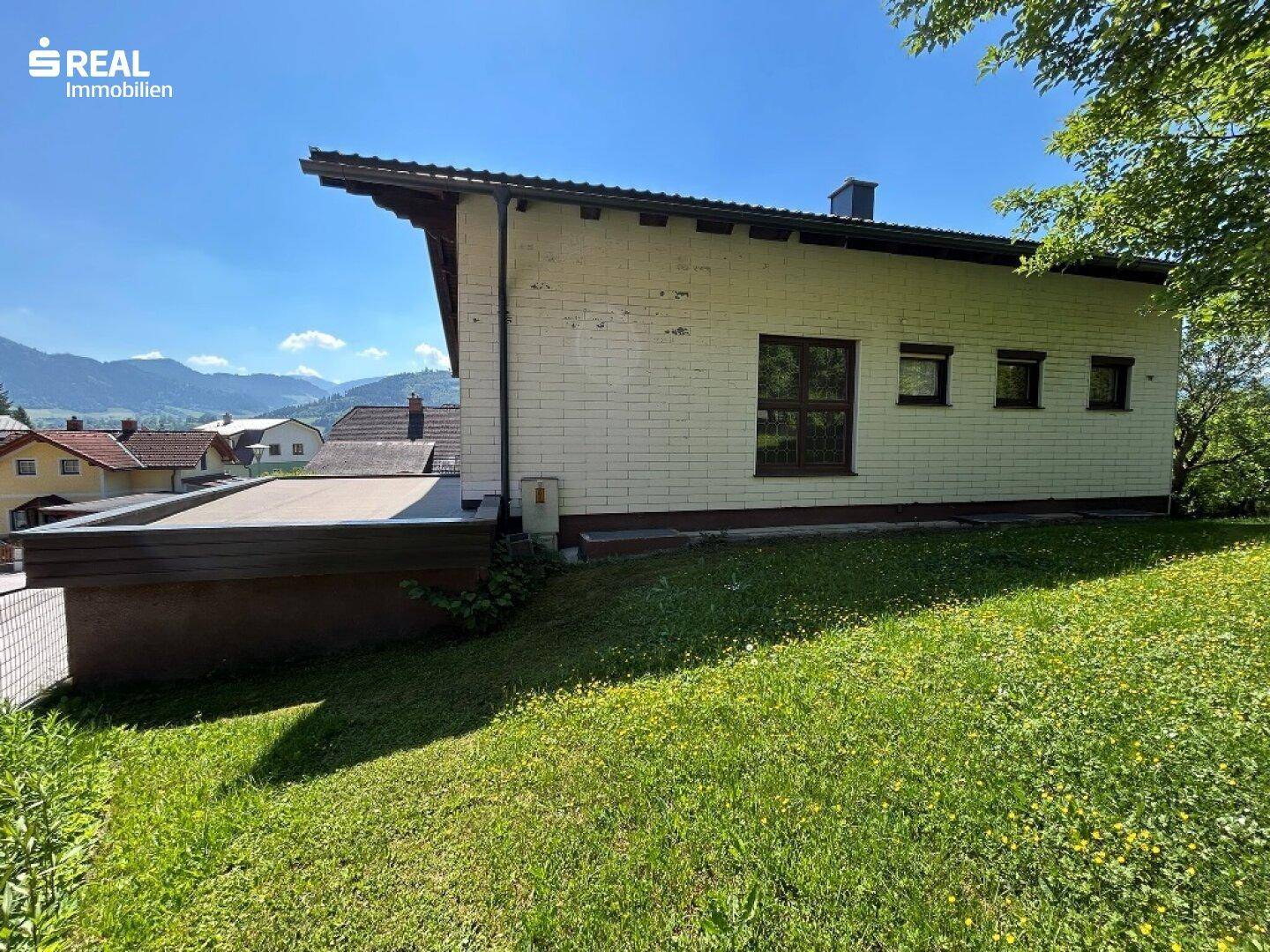 Seitenansicht des Hauses mit weißer Fassade, Flachdachanteil und weitläufiger Rasenfläche.
