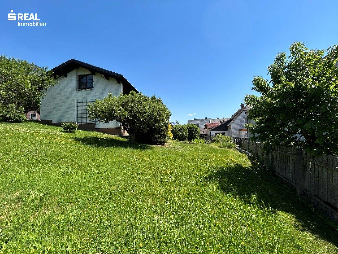 Große, sonnige Rasenfläche im Garten mit Blick auf das Haus und die grüne Umgebung.