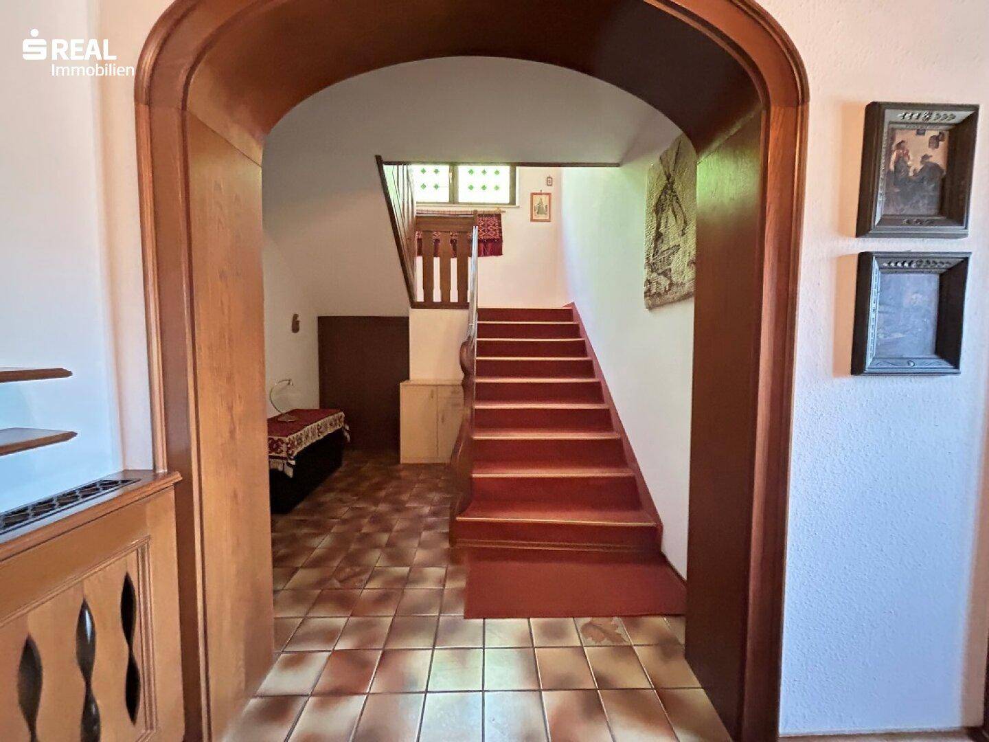 Eingangsbereich mit rustikalem Holzbogen und Treppe zum Obergeschoss, gefliester Boden.