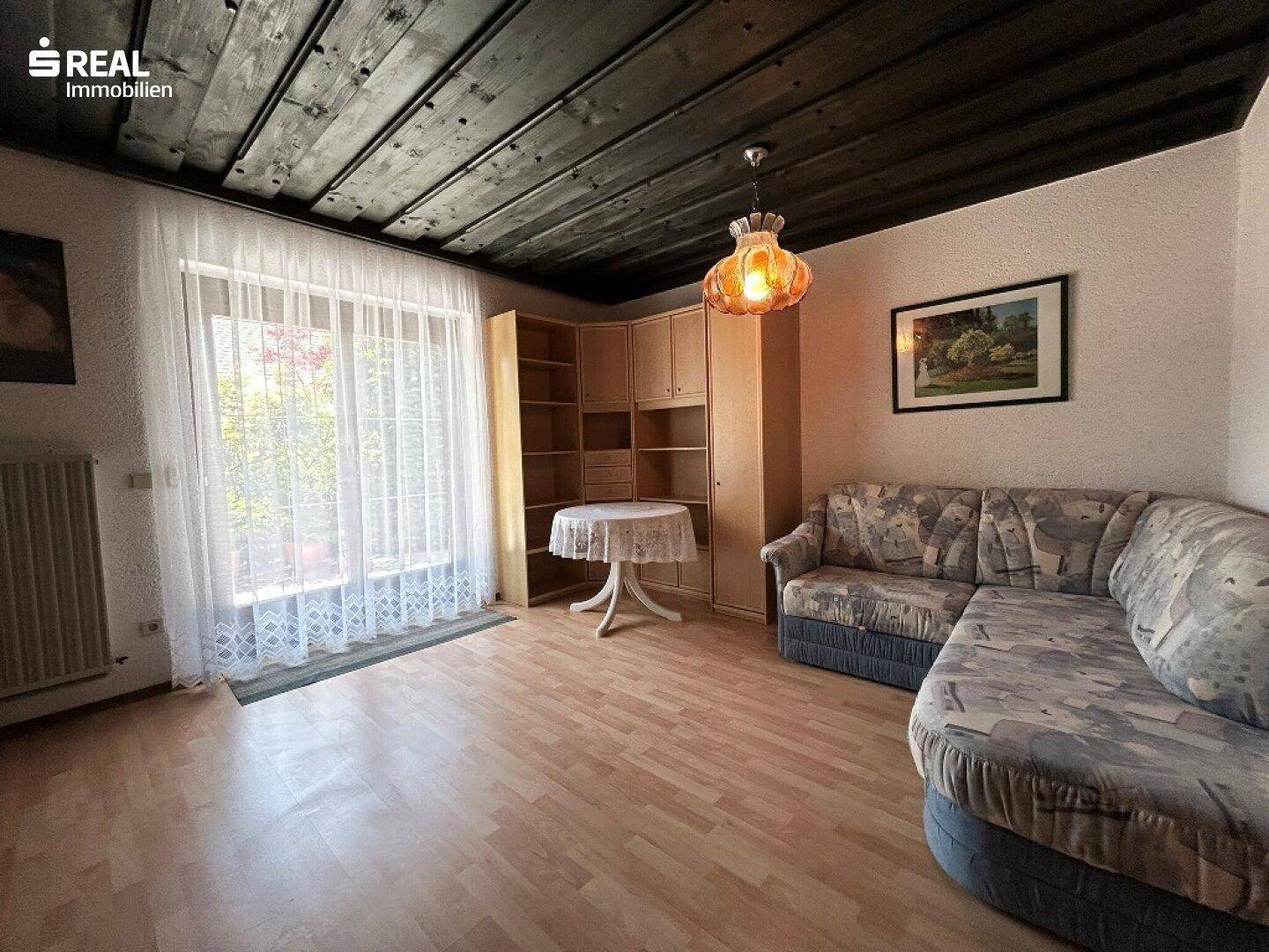 Gemütliches Wohnzimmer mit Sofa, Holzdecke und Zugang zum Balkon oder Garten.