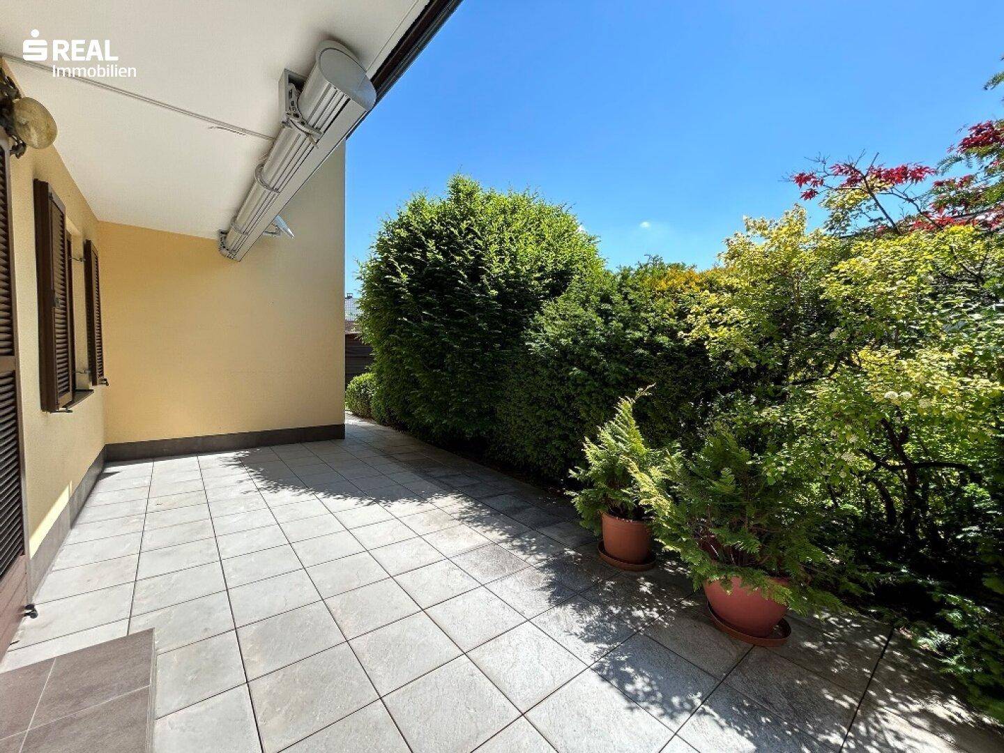 Geräumige, geflieste Terrasse mit Markise und Blick ins Grüne, ideal für Mahlzeiten im Freien.