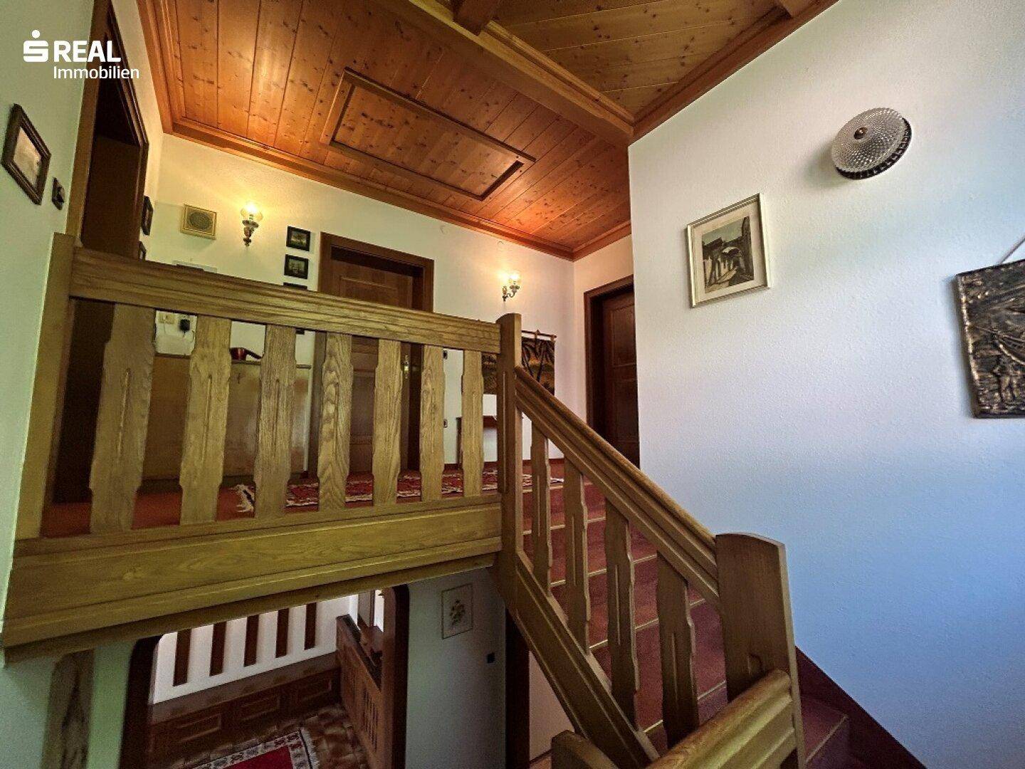 Traditioneller Treppenaufgang mit Holzgeländer und Holzbalkendecke, der zu den oberen Etagen führt.