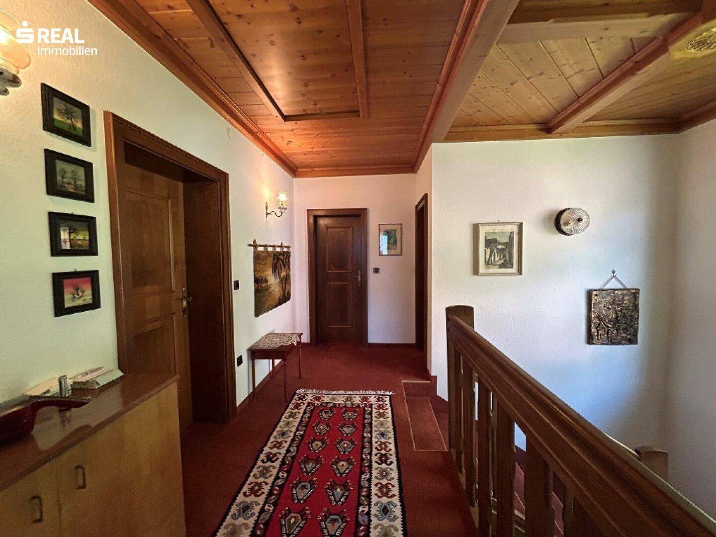Gemütlicher Flur im Obergeschoss mit rotem Teppichläufer, Holzbalkendecke und traditionellen Türen.