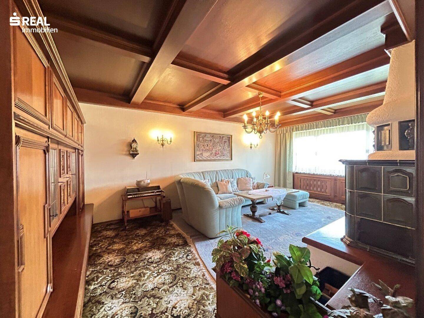 Geräumiges Wohnzimmer mit traditionellem Kachelofen, Holzbalkendecke und gemütlicher Sitzecke.
