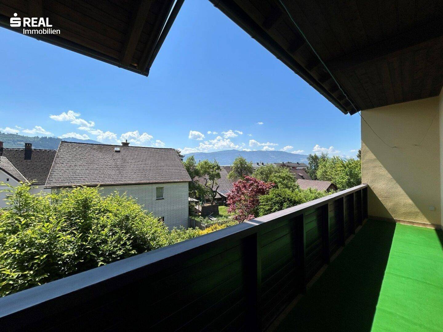 Balkon mit Kunstrasen und weitem Blick über die Dächer der Nachbarschaft bis zu den Bergen.